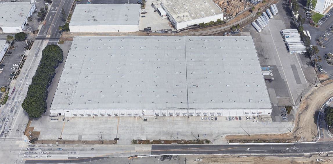 Top view of a big building with a white roof that is surrounded by cars parked in the lot around it.