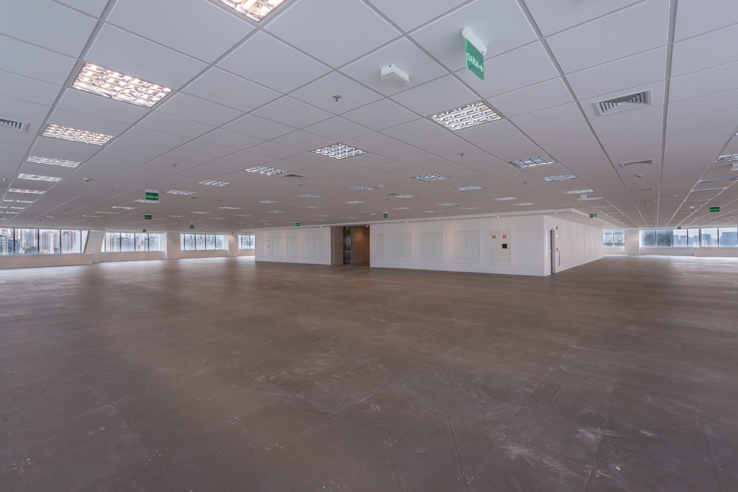 A large empty room with white ceiling panels and walls that has windows lining the sides.