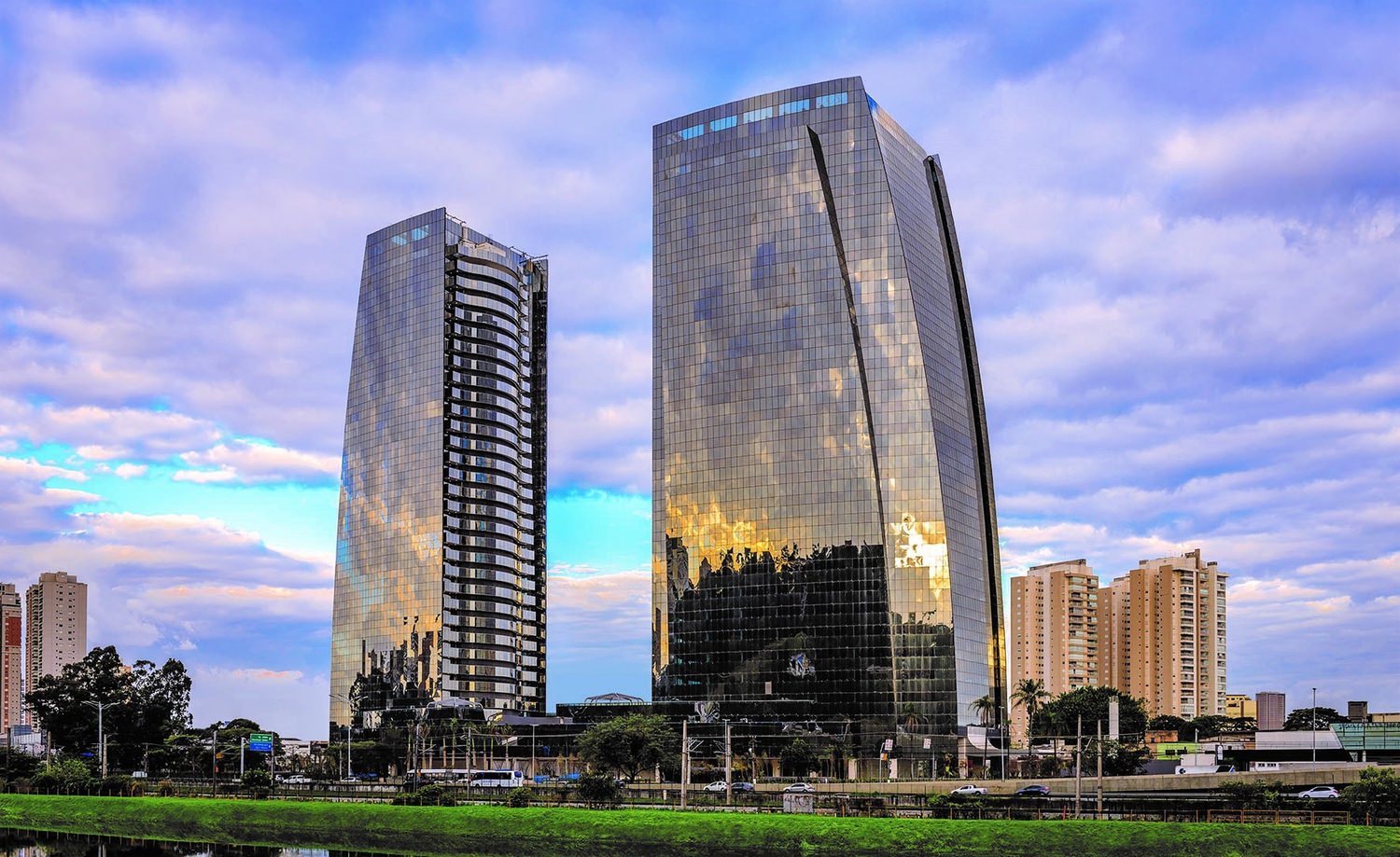 A row of tall skyscraper buildings with clouds in the blue sky in the background.
