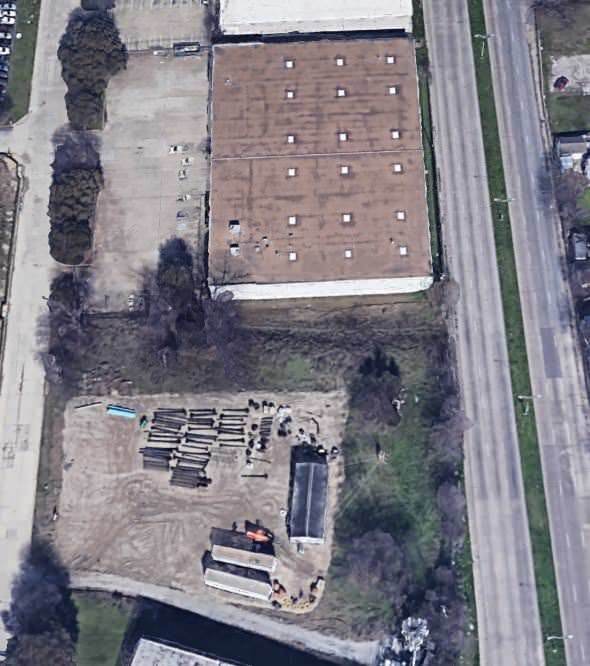 Top view of a building with a brown roof and cars parked in the lot next to a road.