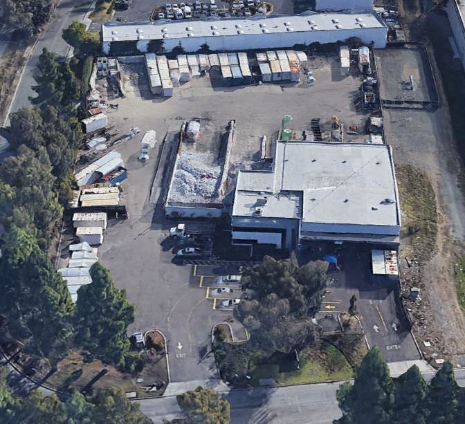 An aerial view of a warehouse and workshop that are near each other with parking lots all the way ar