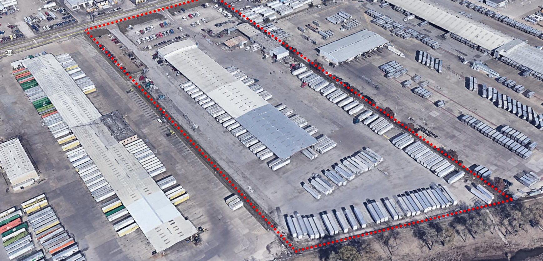 A warehouse that has a lot of semi trucks parked in the parking lot around it and containers behind