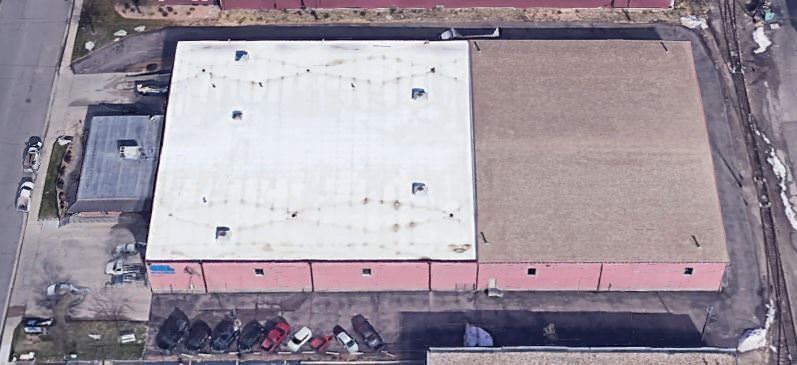 A warehouse that has a parking lot around it with cars sitting next to it and a road to the left of