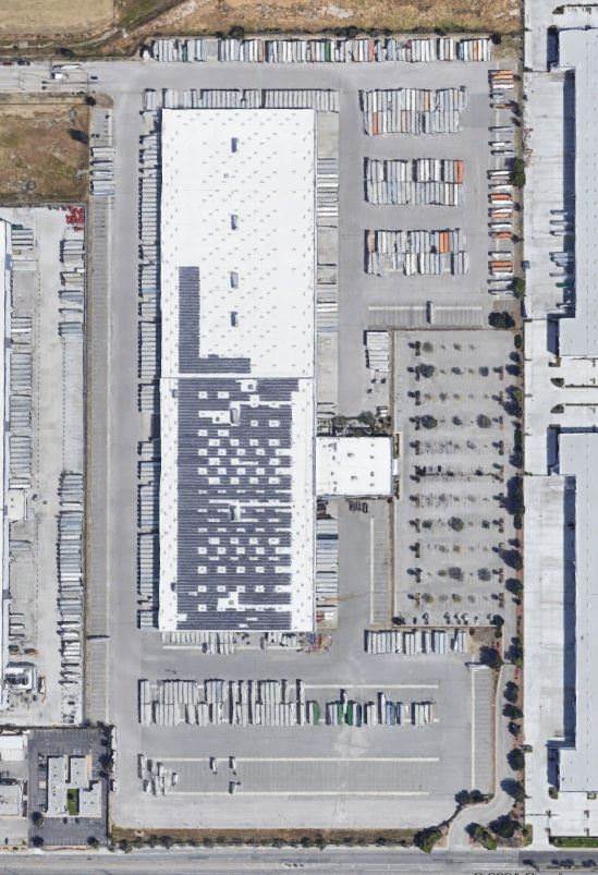 Top view of a white warehouse that is surrounded by a parking lot full of cars and trucks.