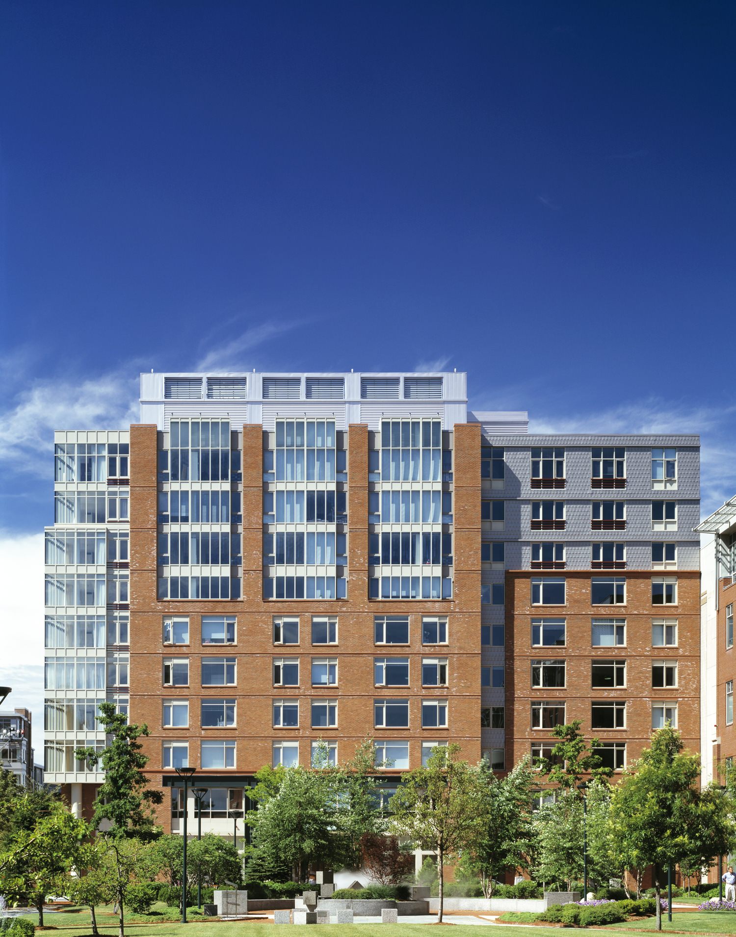 A large brown building with a lot of windows that has a grass lawn and trees in front of it.