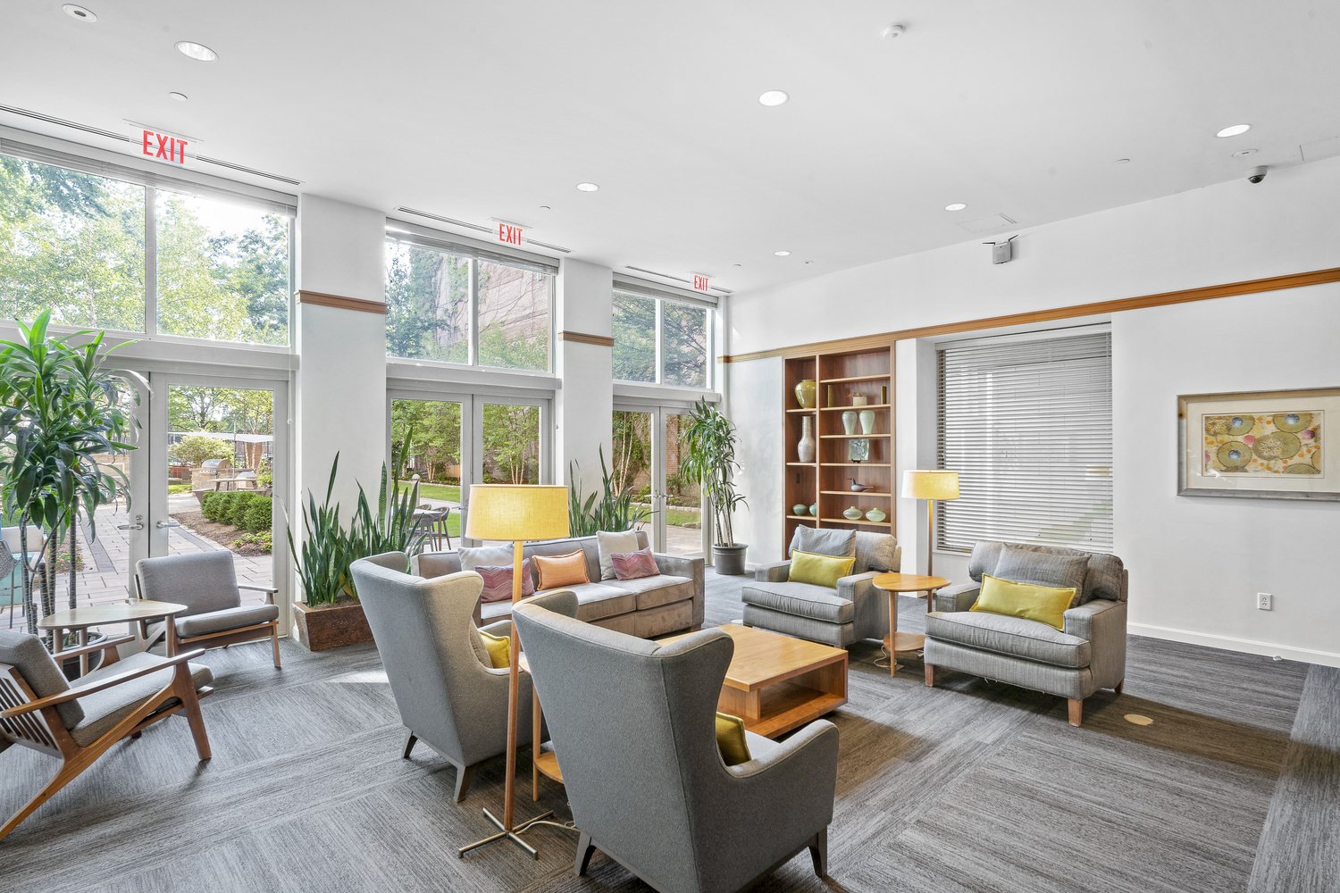 Lobby inside a building that has grey couches and other furniture with a glass wall that gives a view of the courtyard.