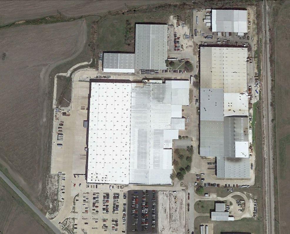 Top view of a group of warehouse with cars and trucks parked in the lot around it.