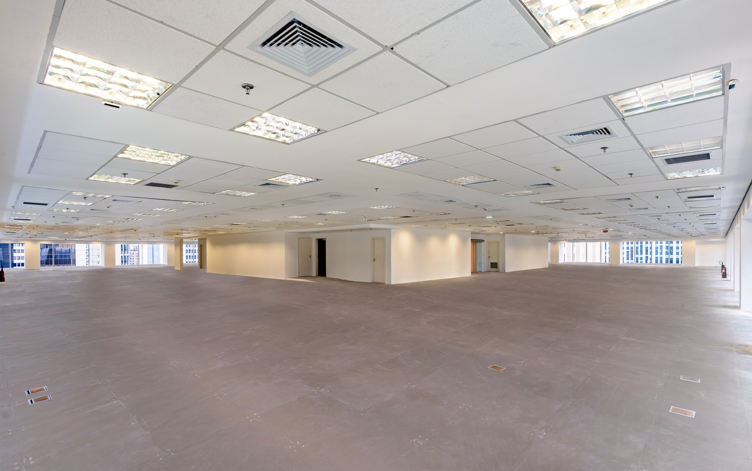 An empty office building that has a white drop ceiling and concrete flooring as well as lighting in the ceiling.