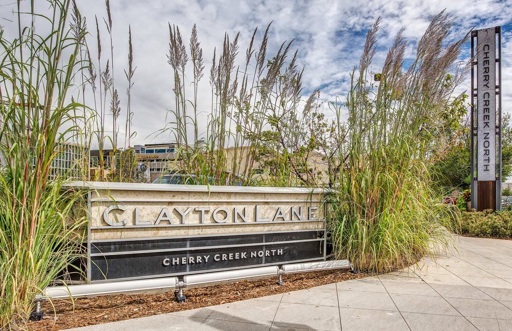 A Clayton Lane Cherry Creek North sign that is surrounded by tall grass om a plaza.