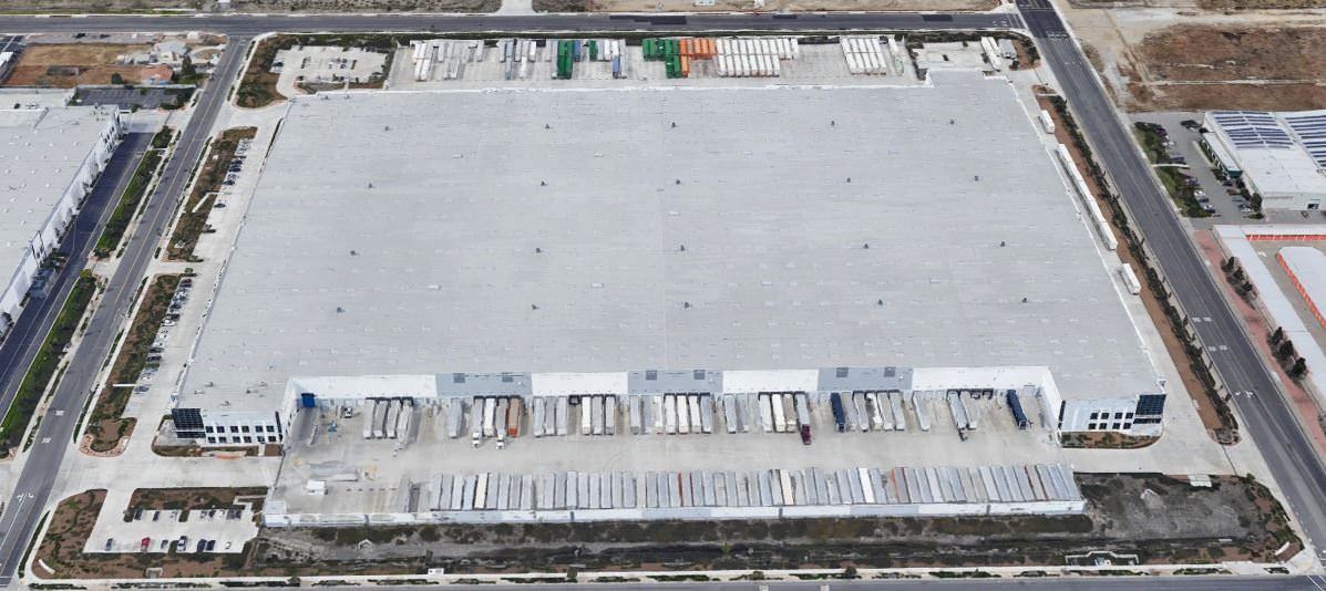 Top view of a large white warehouse building that has trucks parked in the delivery area.
