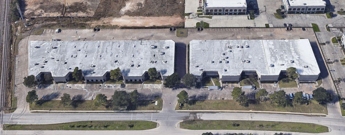 A few white old buildings with grey roofs has cars parked in the area around it.