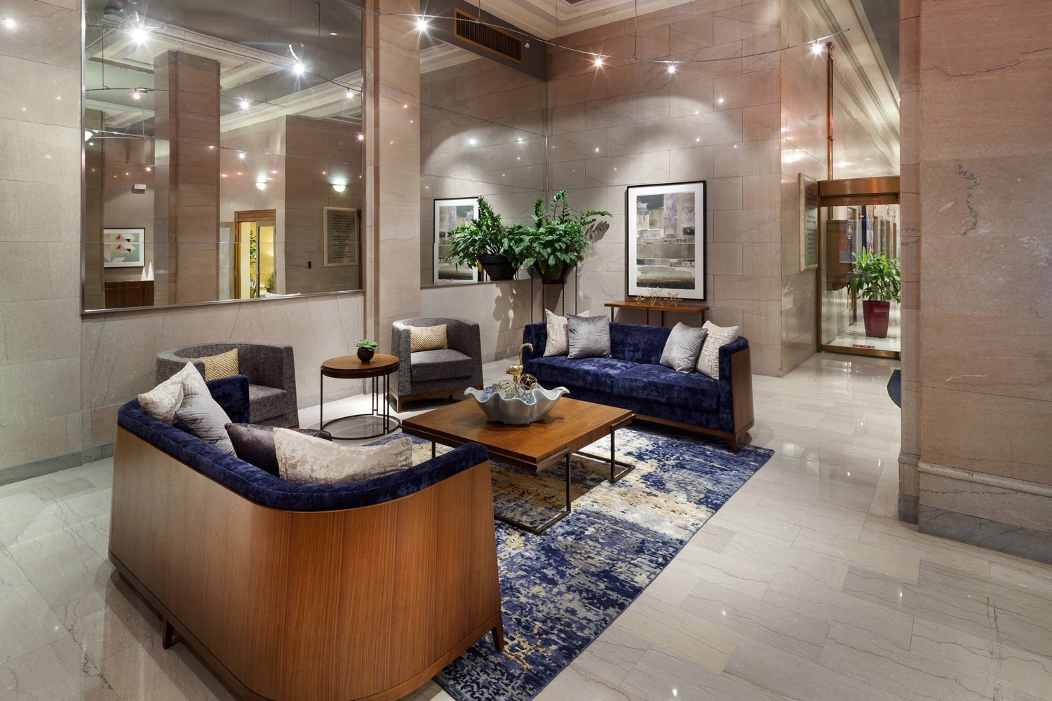 Lobby of a building that has tables and couches in the middle of it with a large mirror on the wall.