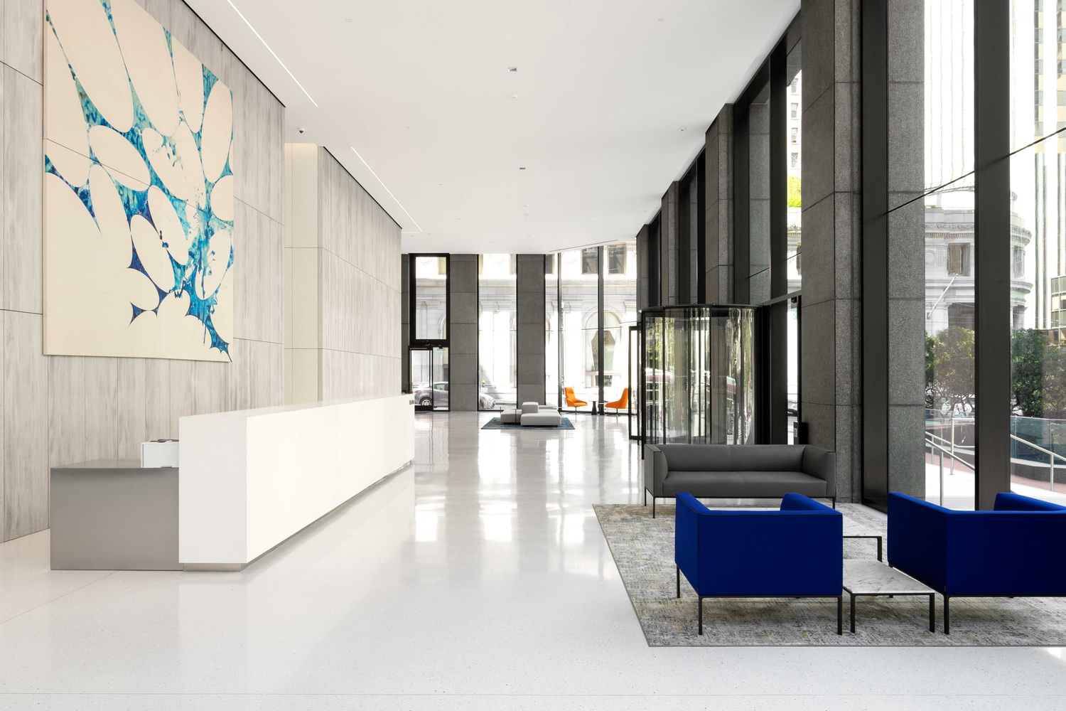 The inside of an office building at the lobby with chairs and a reception desk with art on the wall behind it.