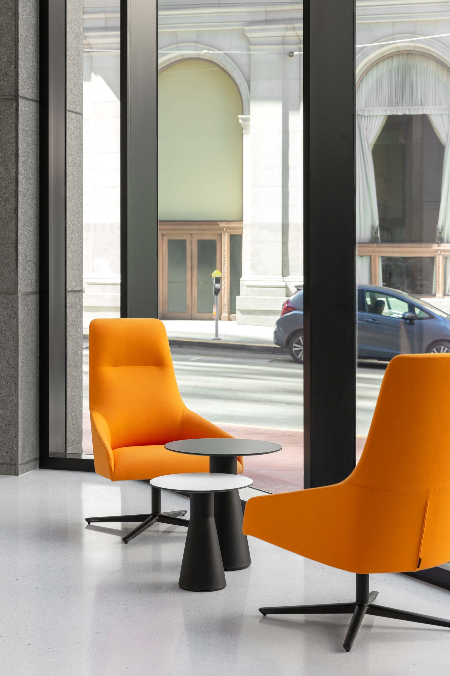 Two orange chairs that are sitting in a lobby around a couple of small tables on a white tile floor.