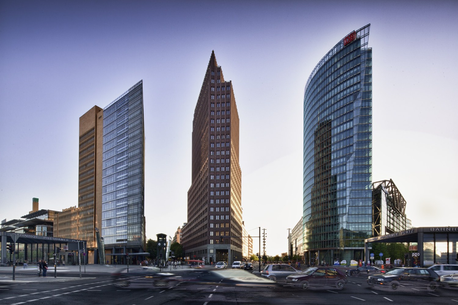 Three buildings that are all near each other with cars that are driving around them in the city.