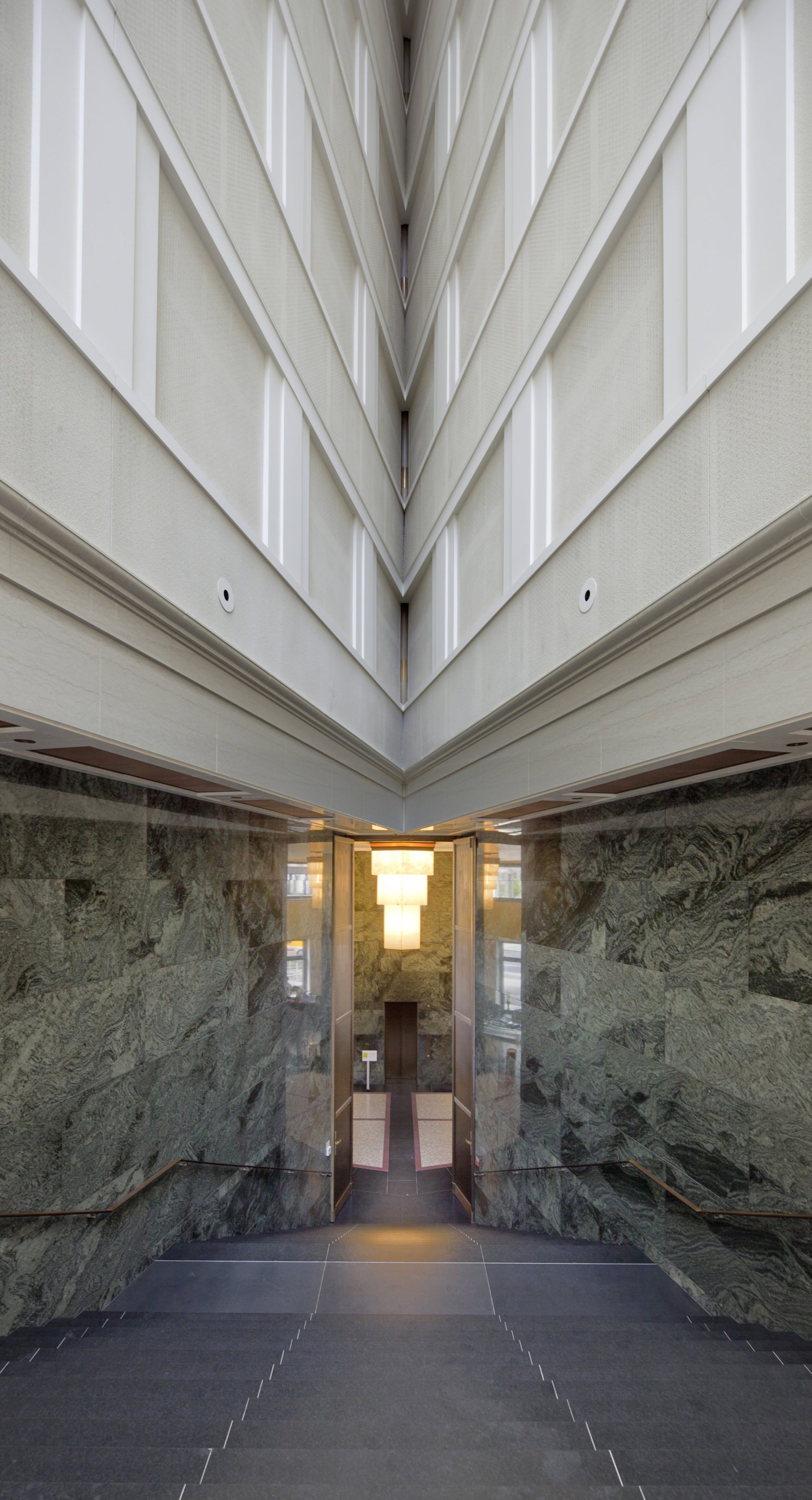 A glass door opens to the sidewalk in a stone room in a building with a white top.
