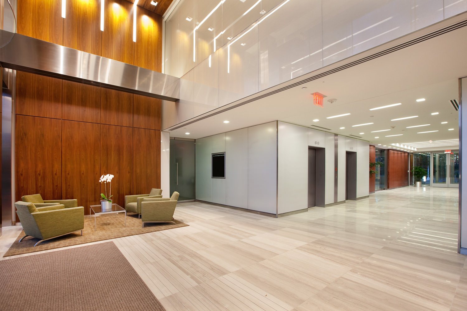 A large lobby of a building that has green couches and wooden panels along the walls.