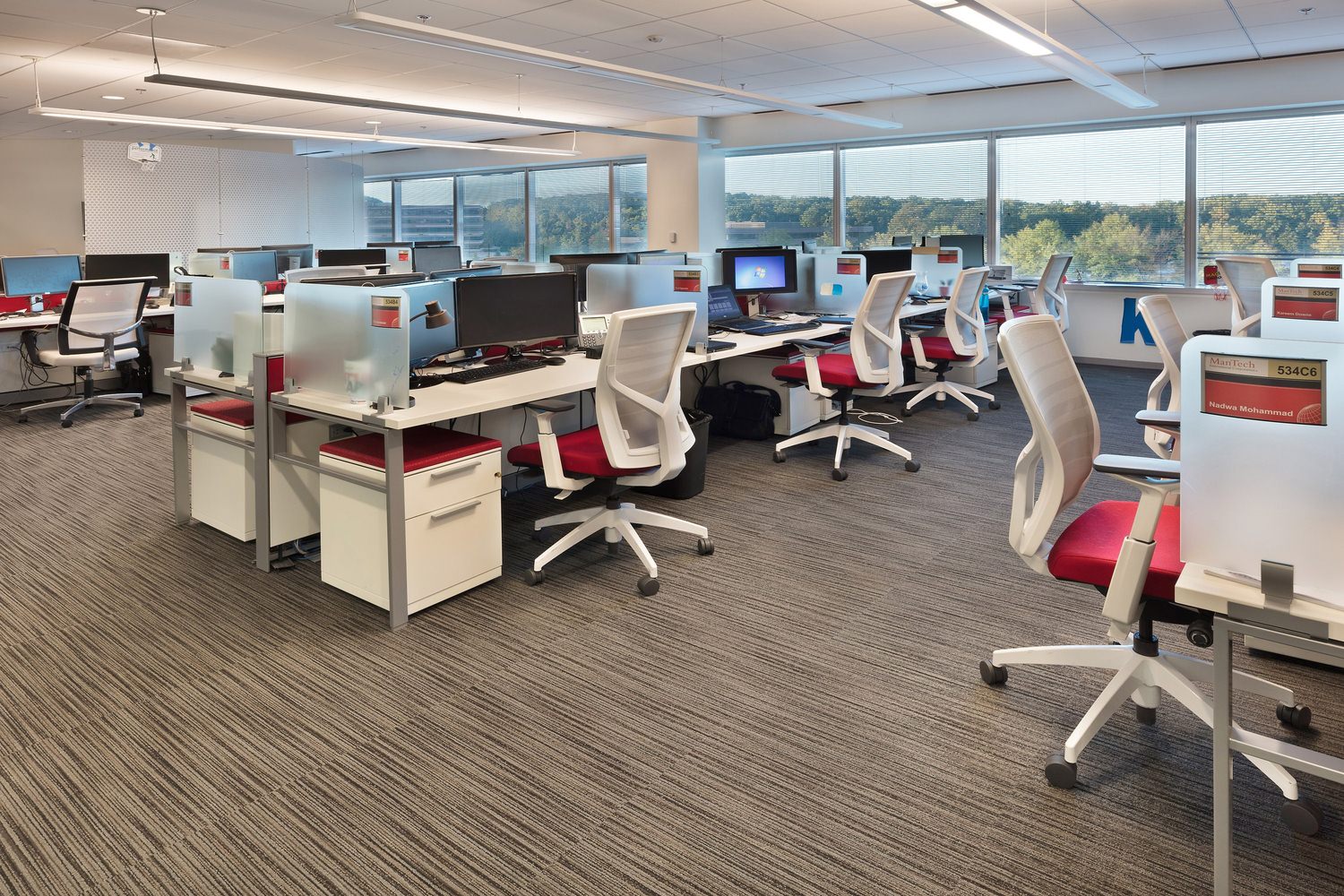 An office where there are desks, computers, and chairs at each one of the desks.