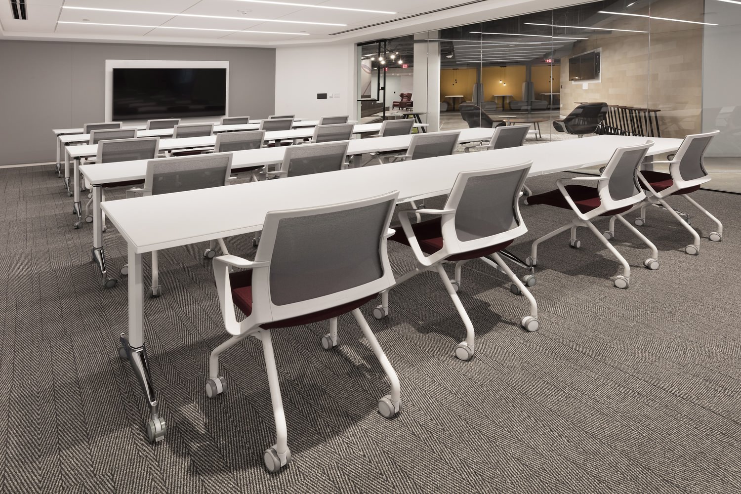 Rows of white tables with chairs inside of a room full of computers and other furniture.