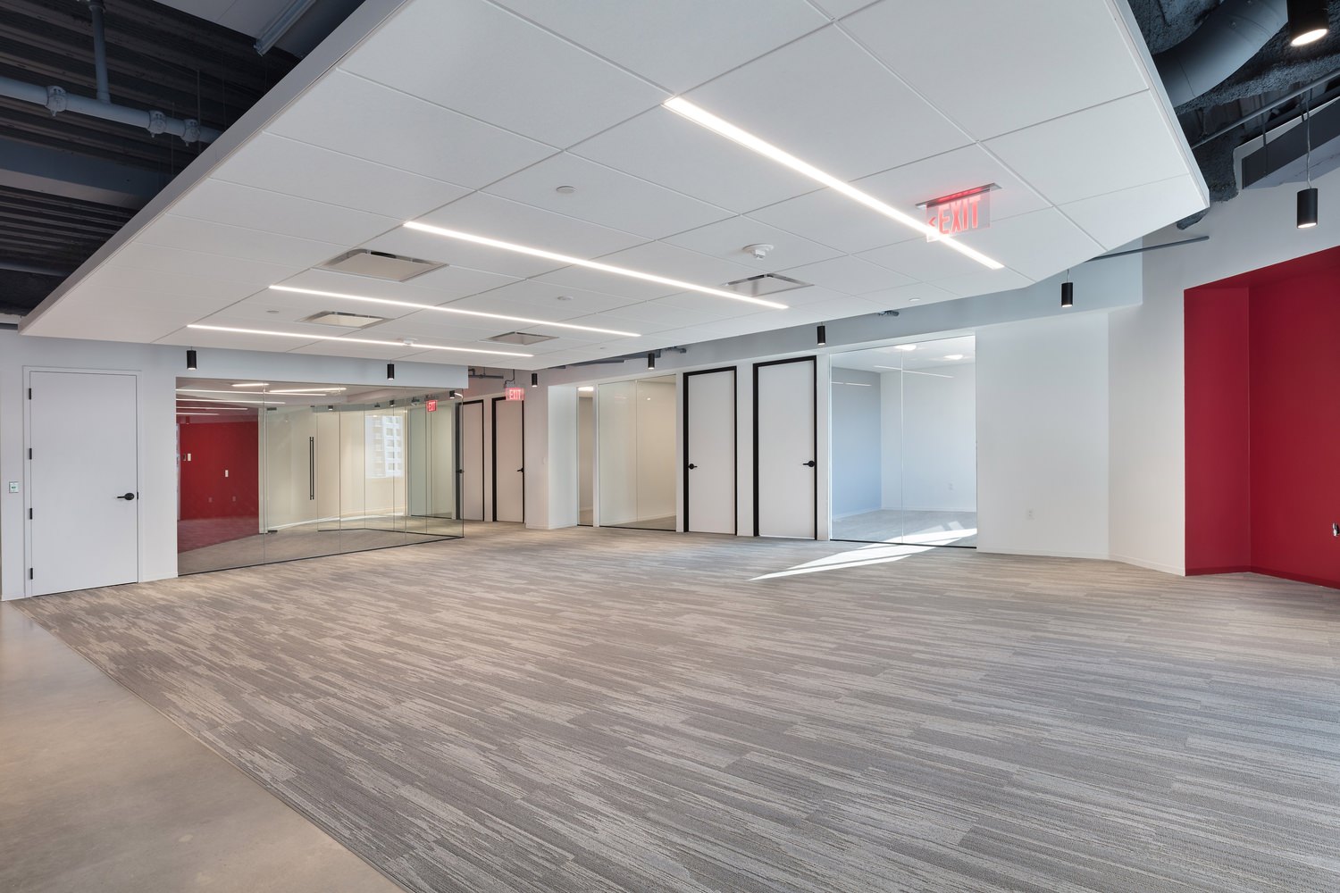 A large room that is empty and has a white drop ceiling in it and wood floors for it.