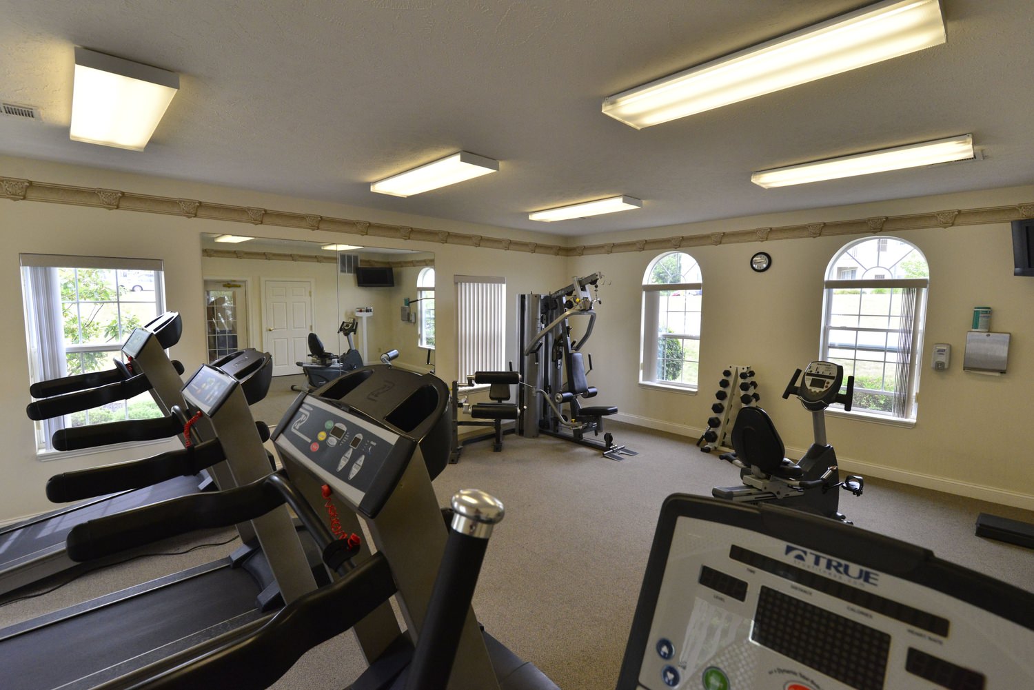 A gym that has treadmills as well as exercise machines in it and some weights in the distance.