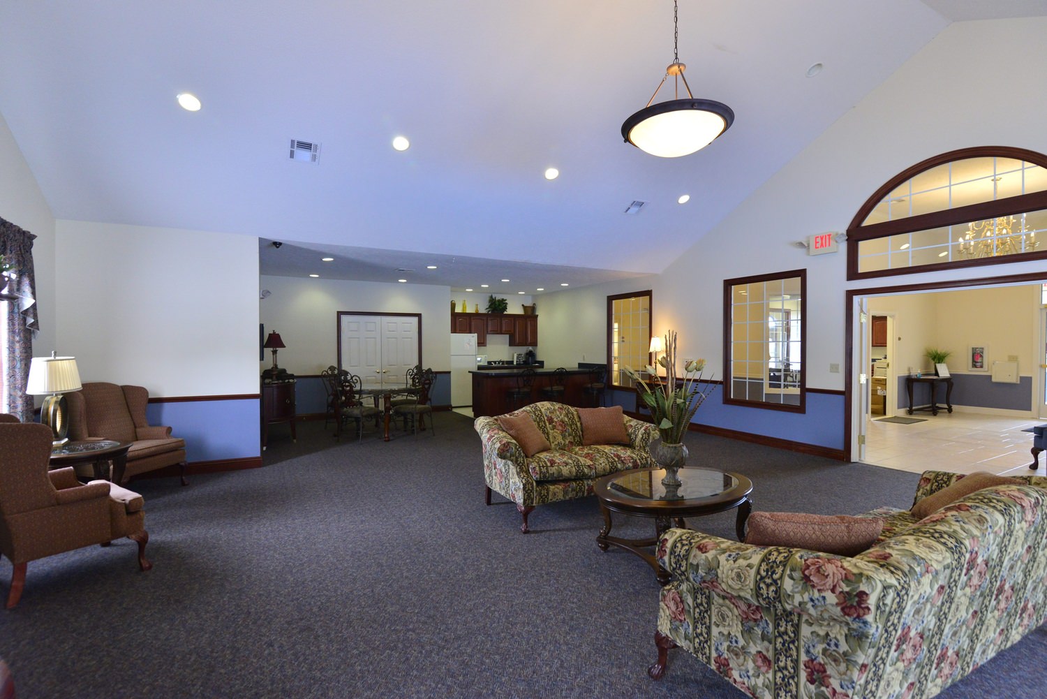 A view of a lobby in a hotel room that has a small bar in the background area of it.