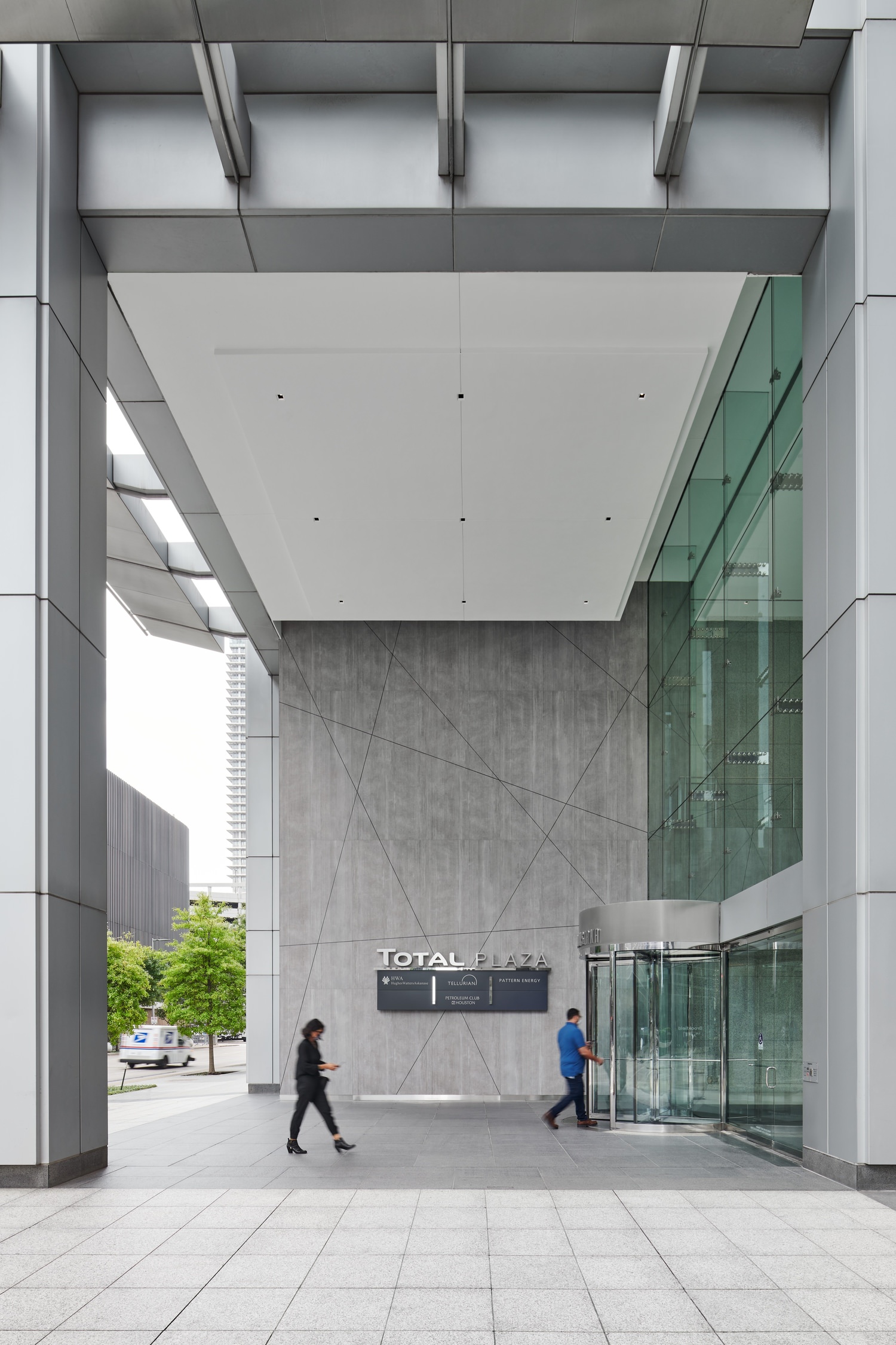 A group of people walking near the front of a large building with glass windows and walls.