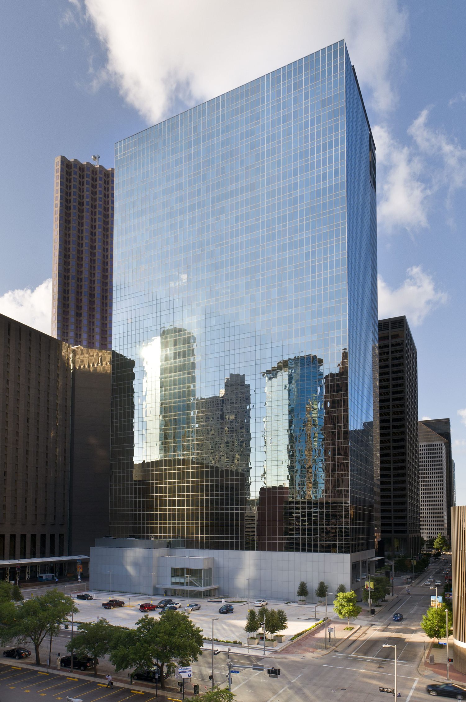 A tall skyscraper that is full of glass windows on the oustide with a plaza next to it.