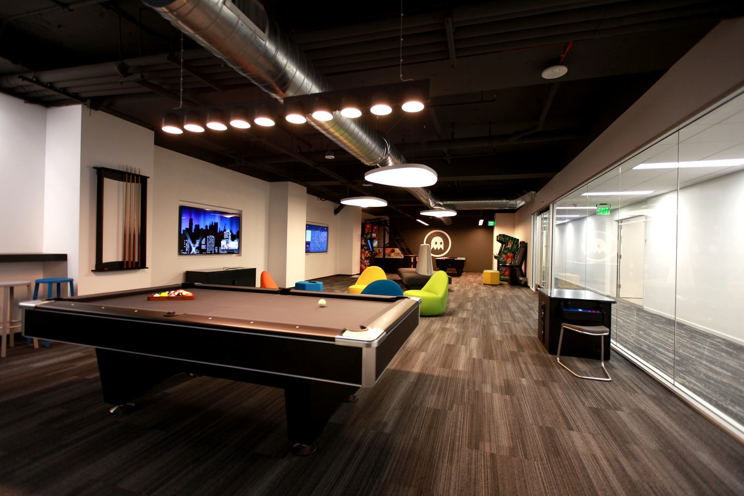 A recreational room with a pool table, arcade games, and lounge seating.