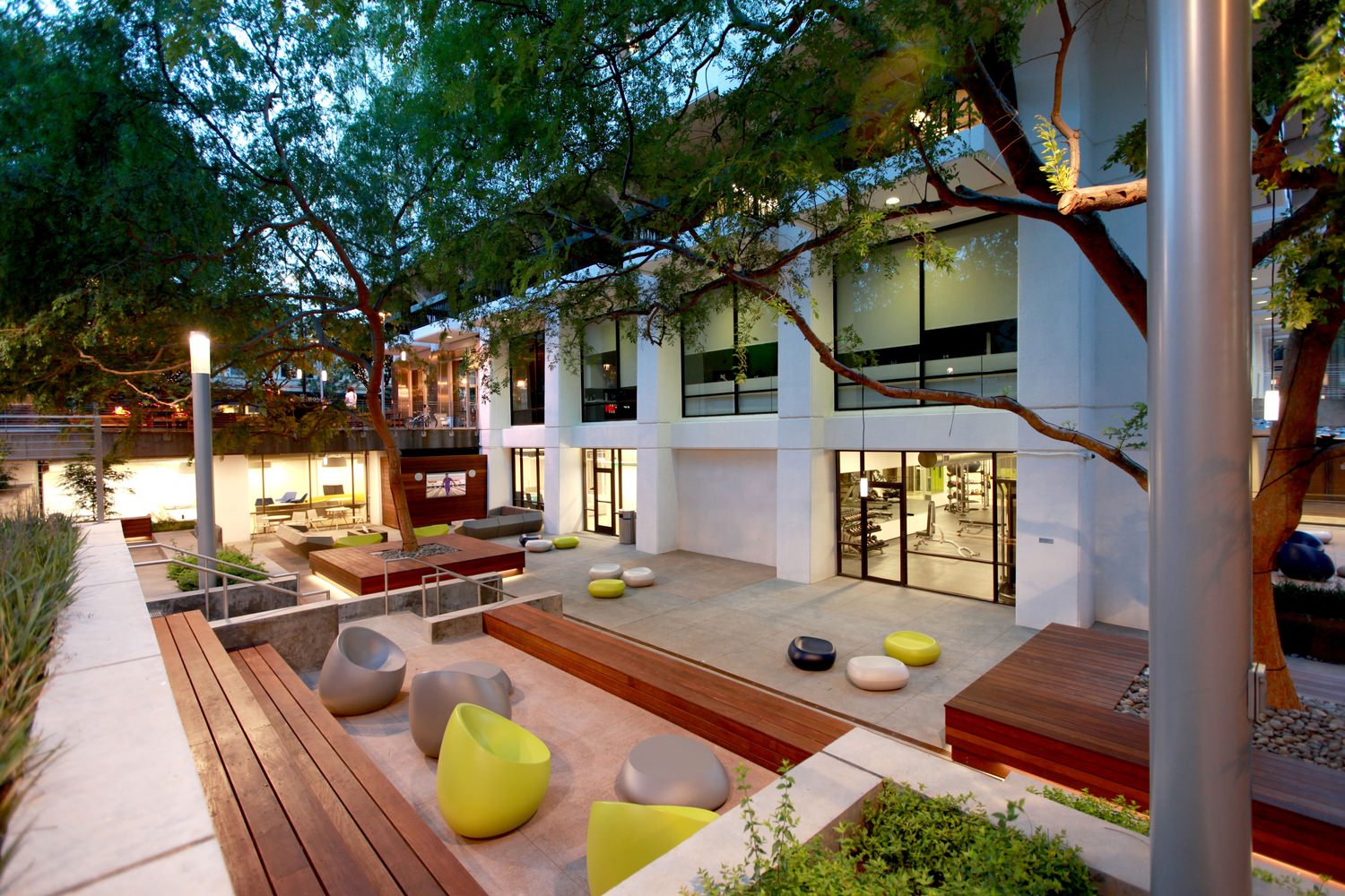 A white building with a courtyard that is full of trees and outdoor furniture along the area.
