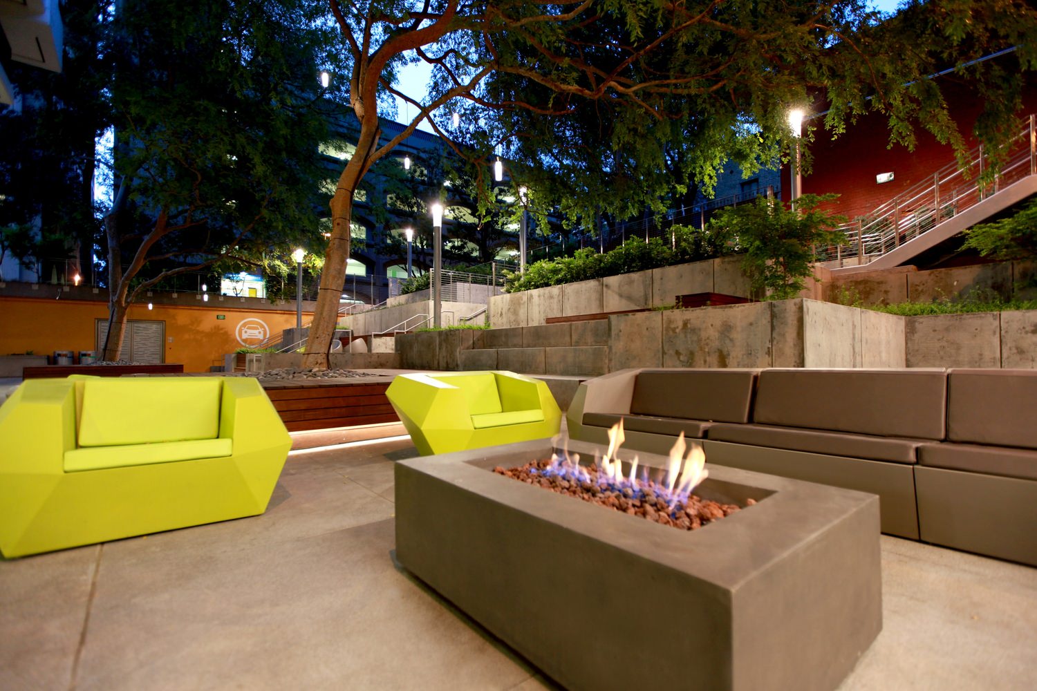 A sitting area features a fire place in a coffee table and many trees surrounding it.