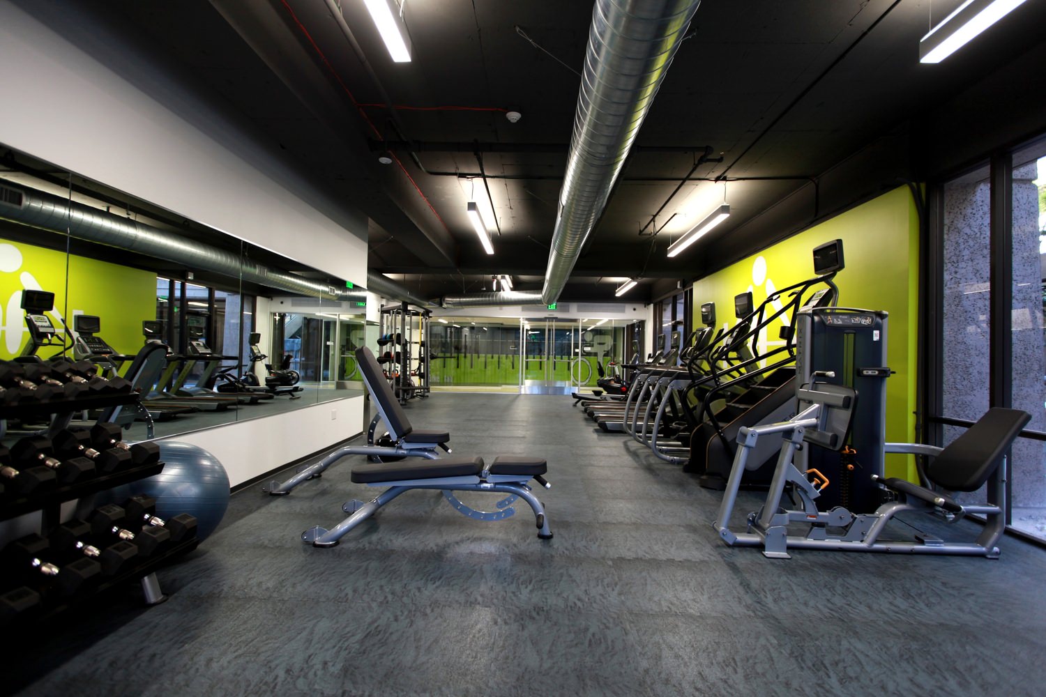 Gym that has a row of stair masters and other exercise equipment next to the walls and mirrors.