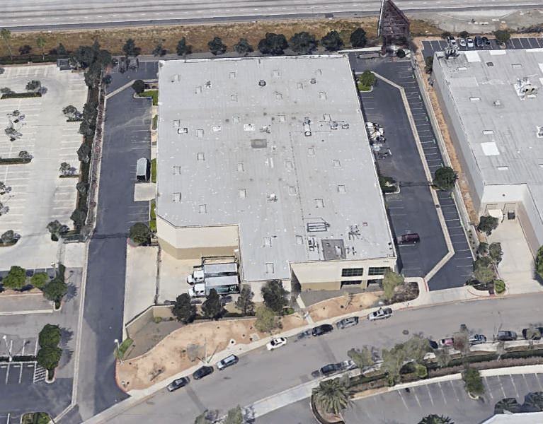 Top view of a few white warehouses that has cars and trucks parked in the lot around it.