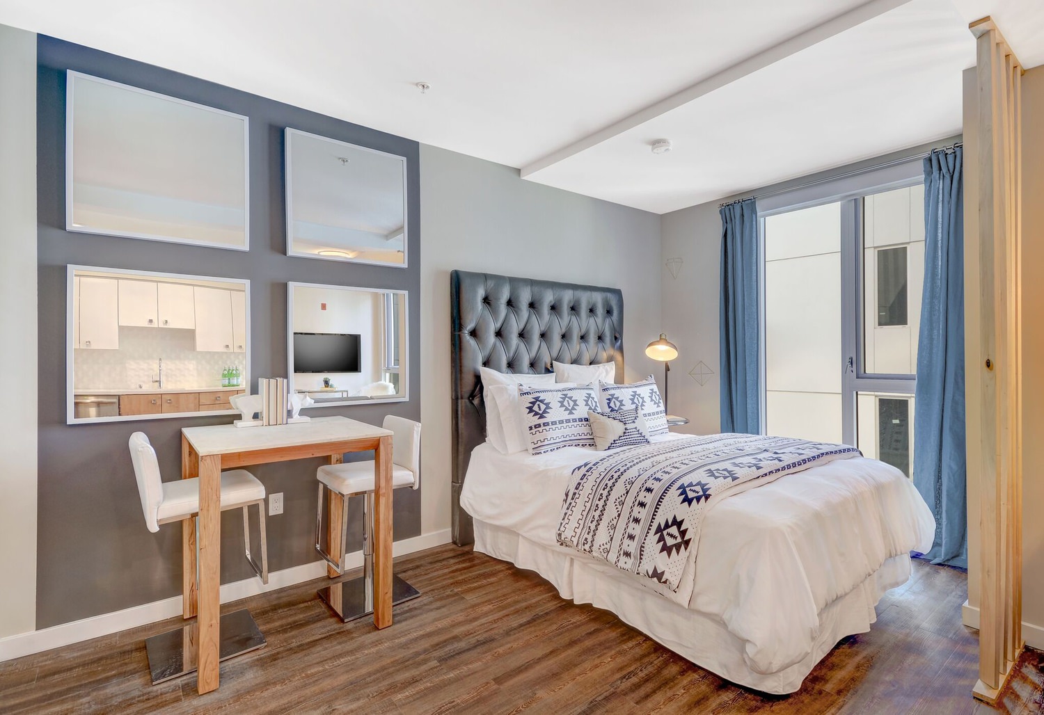 A bedroom with a a desk and chair that is next to a bed covered in white linens.