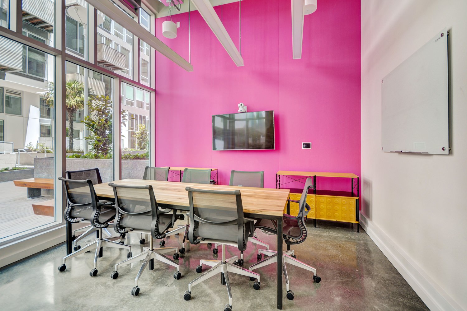 An office with a long table that is surrounded by chairs and next to a pink wall.