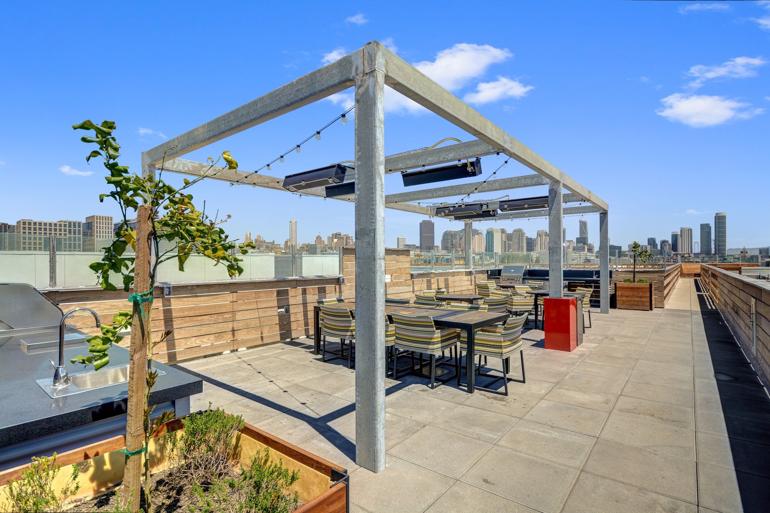 A rooftop patio with tables and chairs setup beneath a pergola strung with lights.