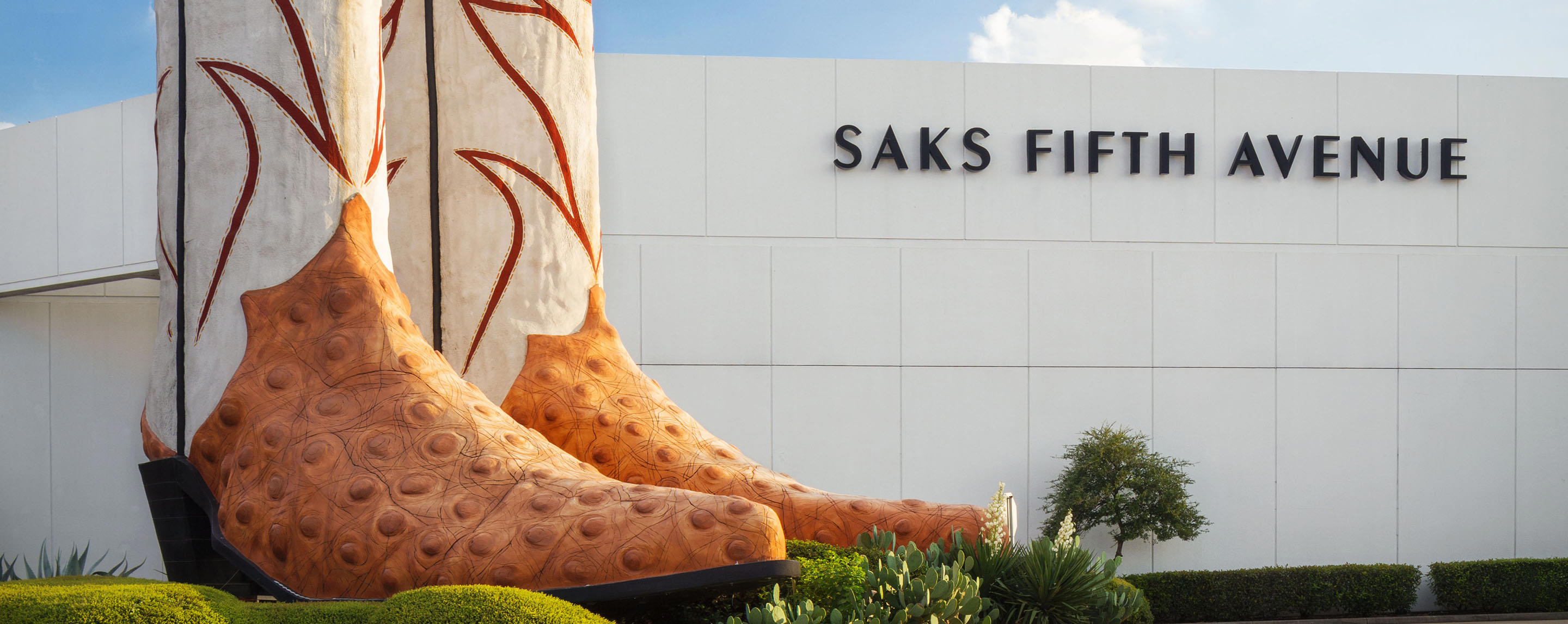 A pair of large boots sits in the foliage near a Saks Fifth Avenue building.