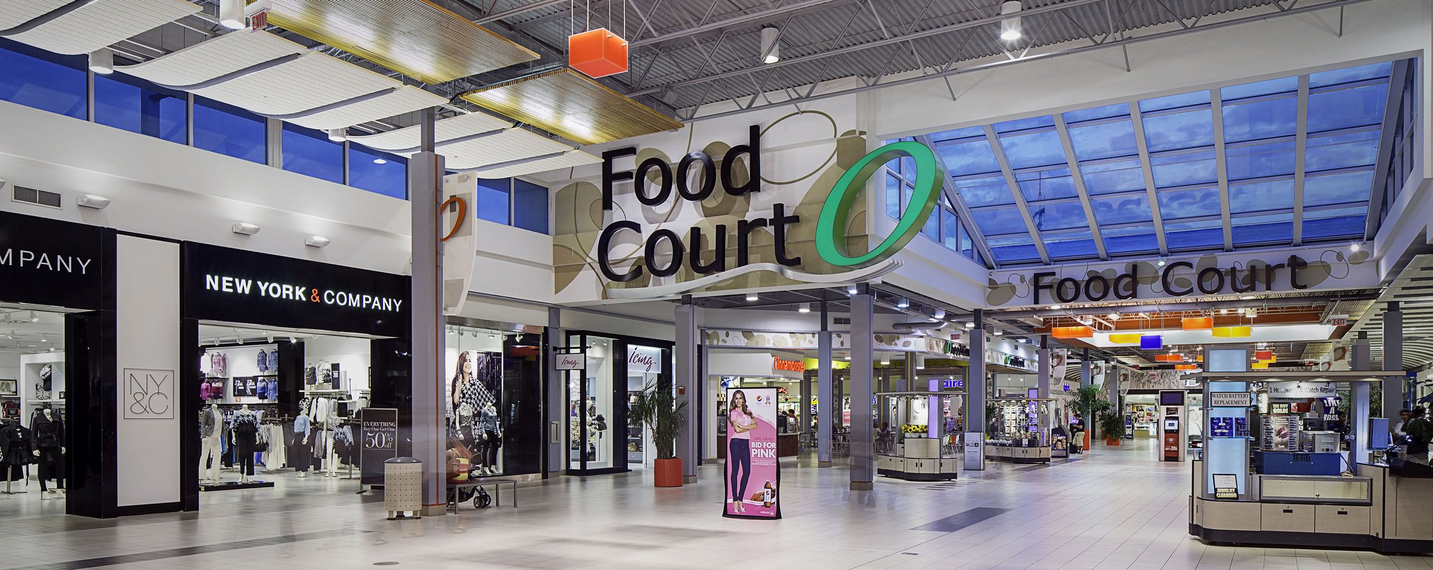 A food court in a mall is filled with kiosks and is located near the New York & Company and PINK