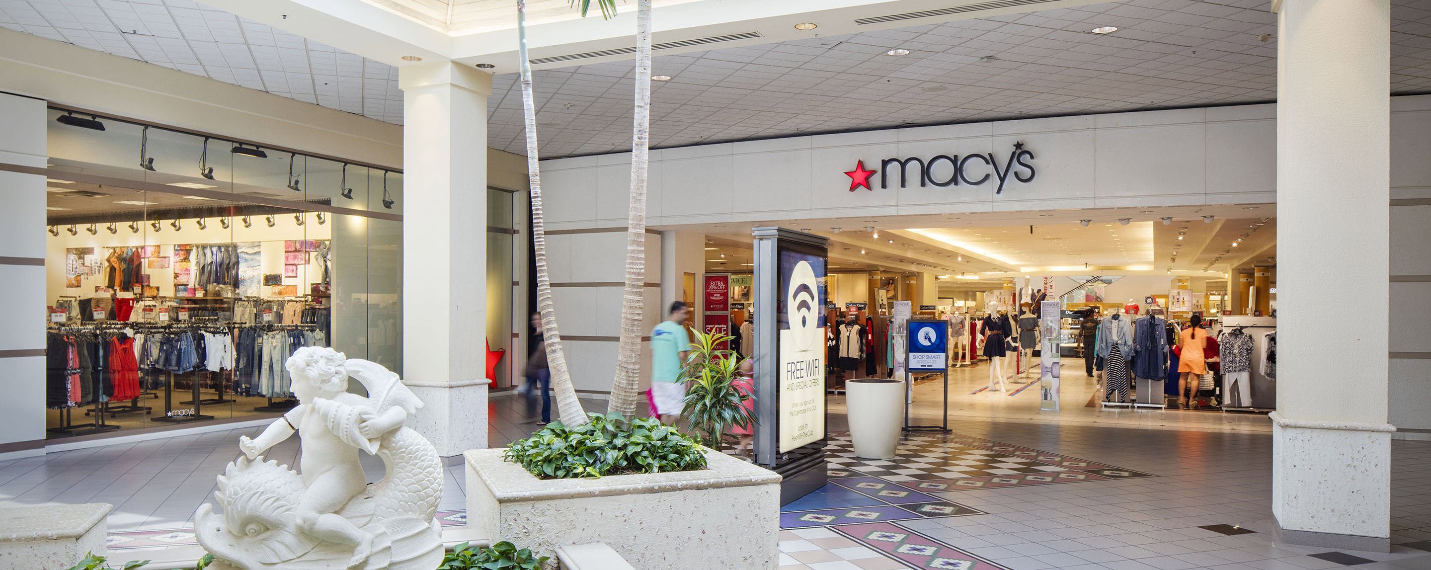 Clothing and items can be seen on display at the entry of a Macy's store in an indoor shopping center.