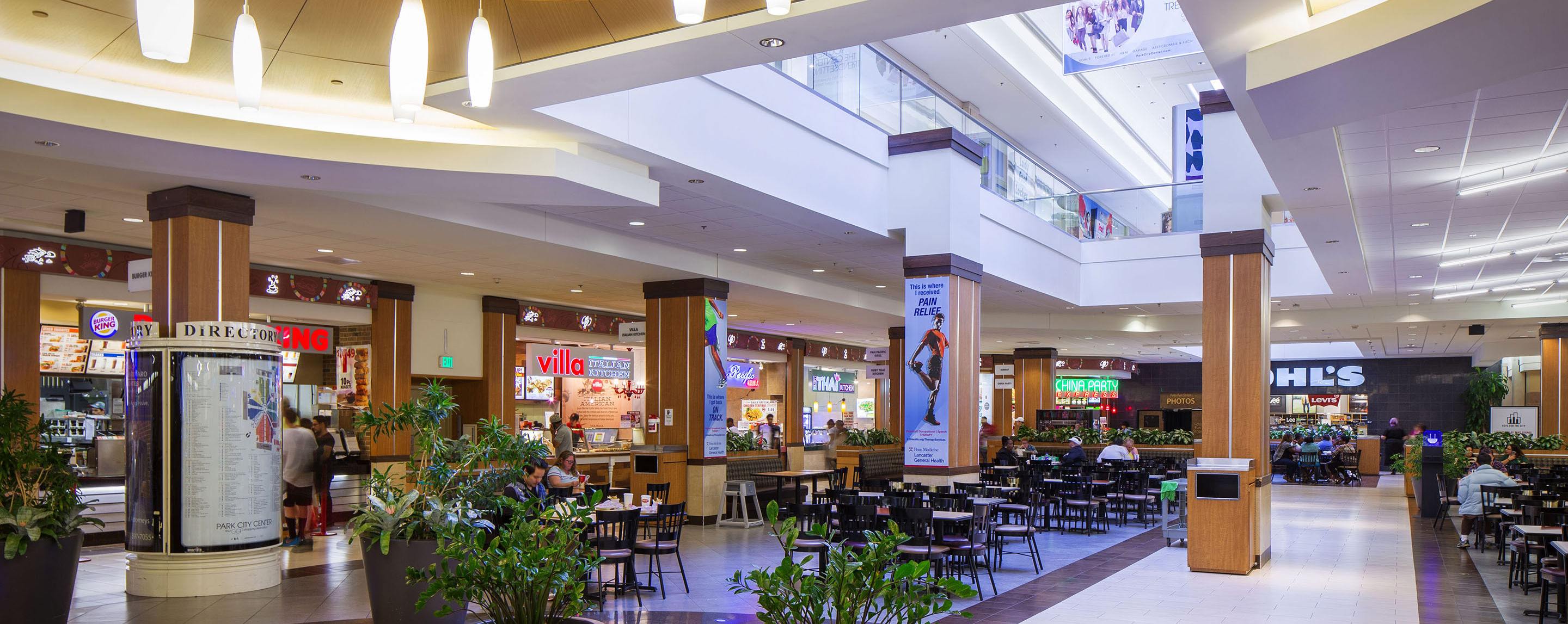 Several rows of empty tables stand in a mall food court. A sign for Kohl's is visible in the background.