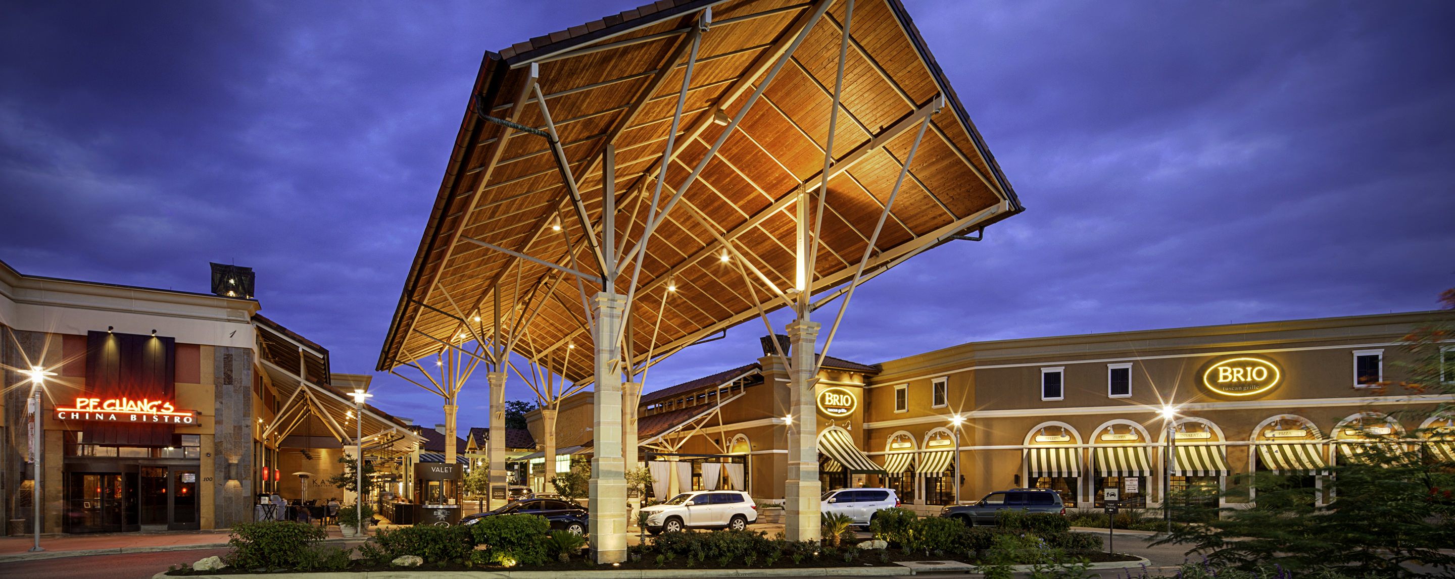A large, well lit awning stands in front of a sprawling building. Several storefronts are visible, including Brio.