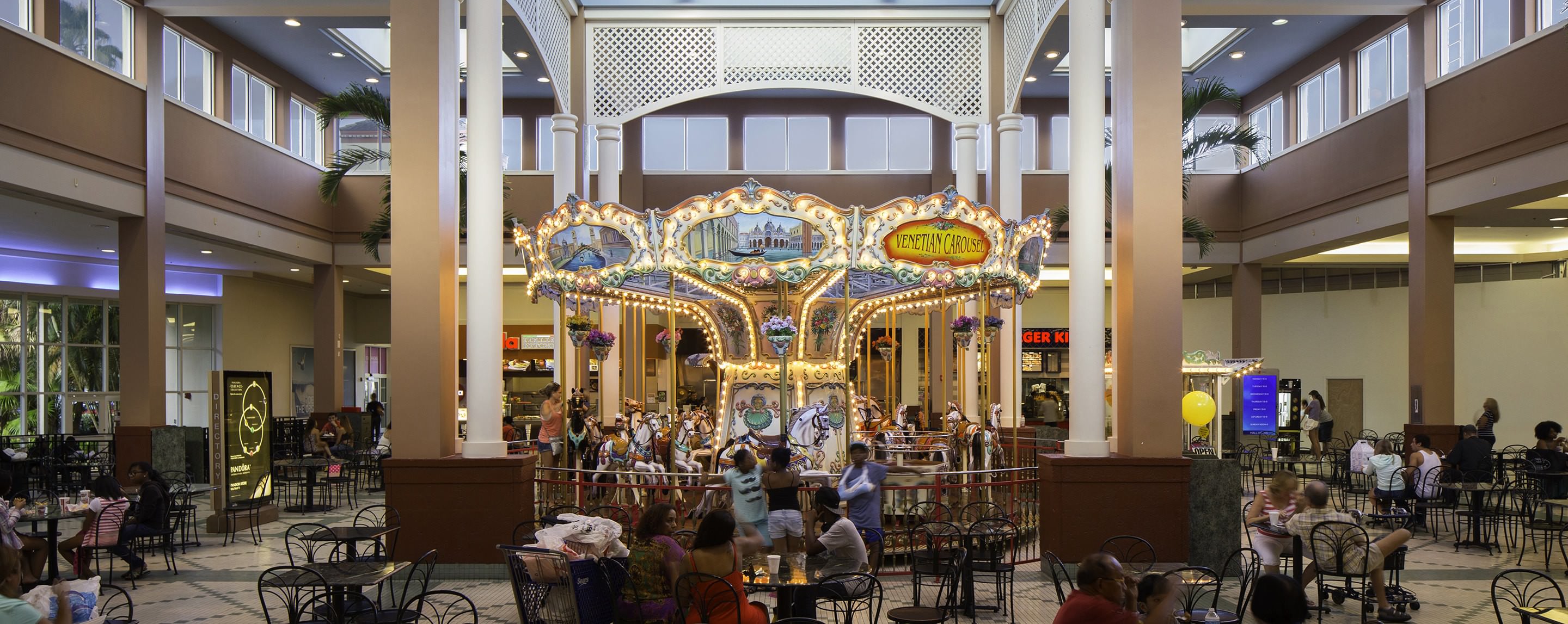A group of tables stands in front of a mall carousel. A Sears storefront is visible.