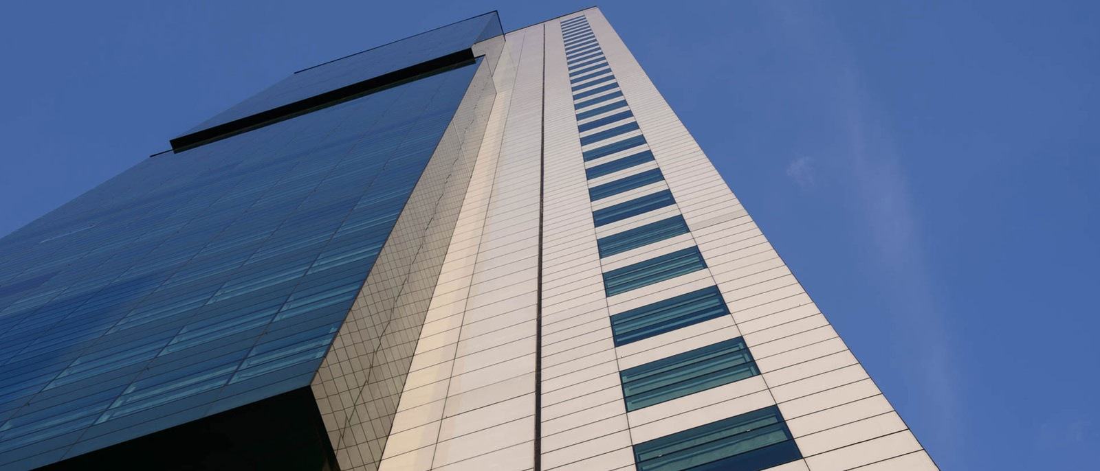 A tall building with brown walls and tinted windows pointing towards the blue sky.