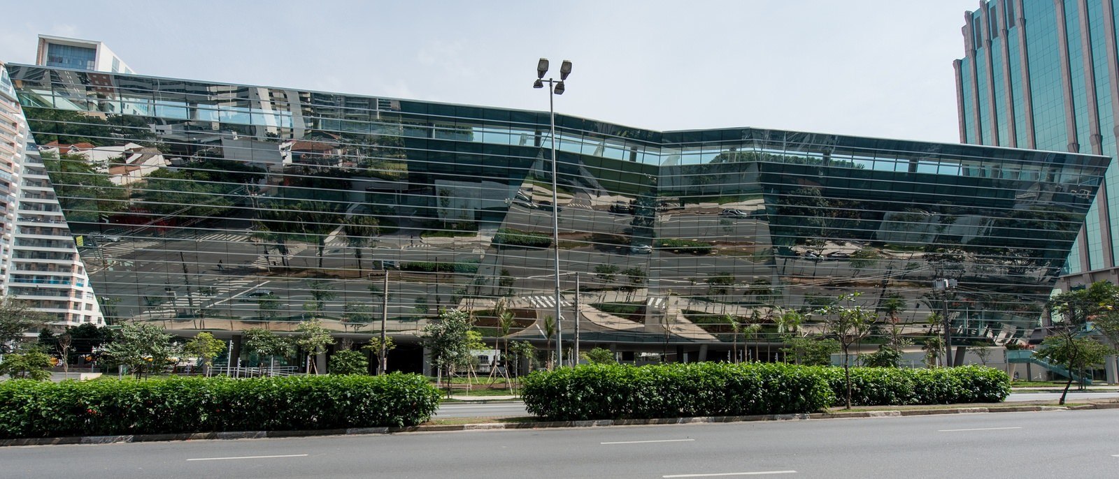 A large building that is covered in glass windows that is next to a sidewalk full of trees.