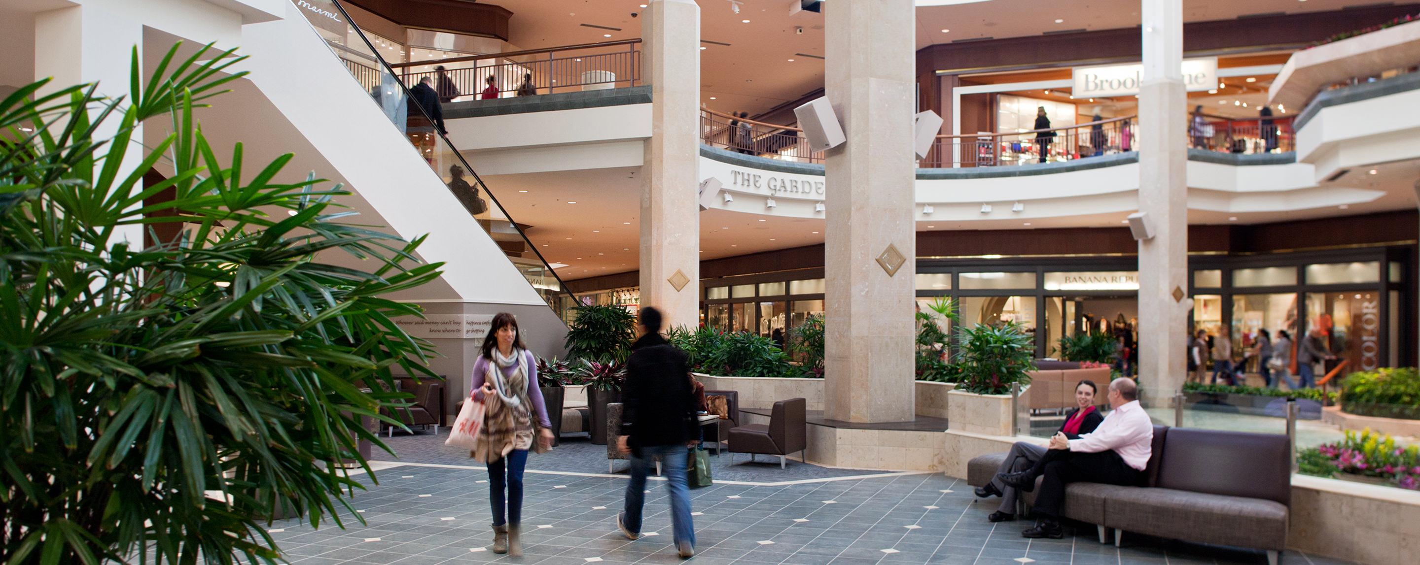 People walk and sit on benches inside of a multi-story mall. A Marmi storefront is visible.