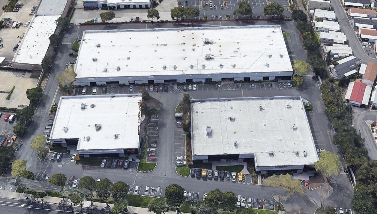 Top view of several building with white roofs that is surrounded by a parking lot full of cars.