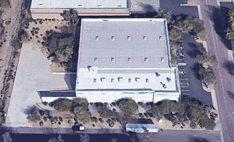 A top view of a building with a white roof that is surrounded by a parking lot full of cars.