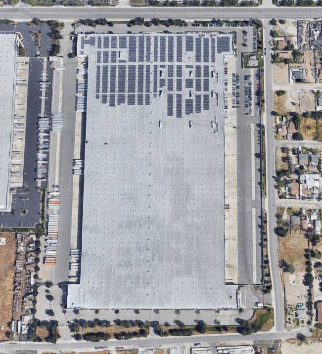 Top view of a warehouse that is surrounded by a parking lot full of trucks and cars.