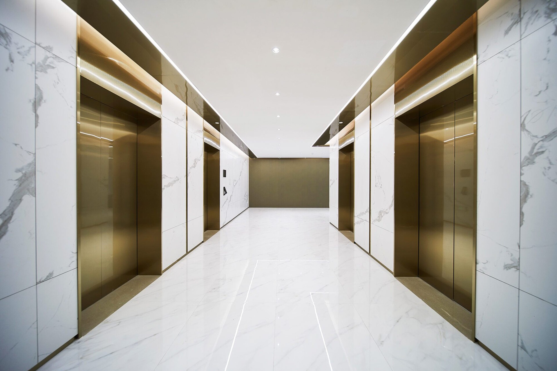 A marbled hallway with four gold elevators.