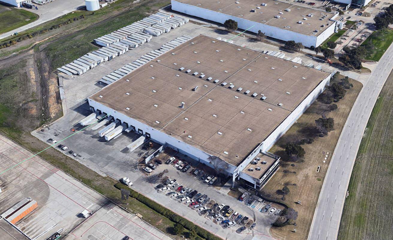 Top view of a large building with a brown roof that has trucks and cars parked in the lot around it.